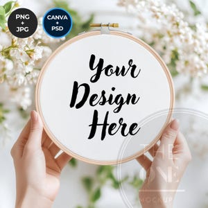 Könnte beinhalten: Ein weißer Stickrahmen mit dem Text "Your Design Here" in schwarzer Kalligraphie. Der Rahmen wird von Händen vor einem Hintergrund aus weißen Blumen gehalten.