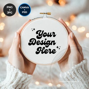 Pode incluir: Um aro de bordado branco com uma moldura de madeira, segurado por mãos. O tecido dentro do aro tem o texto "Your Design Here" escrito em preto.