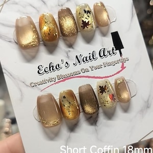 Op de afbeelding: Een set van tien korte doodskistvormige press-on nagels in goud-, brons- en crèmetinten, voorzien van glitters, metallic folie en herfstbladaccenten. De displaykaart vermeldt Echo's Nail Art, Creativity Blossoms On Your Fingertips, Short Coffin 18mm.