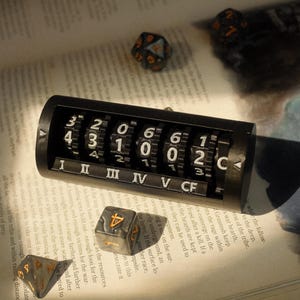 May include: A black counter with six rotating dials, each with numbers from 0 to 6. The counter is labeled with Roman numerals I through V and CF. The counter is sitting on a book with dice scattered around it.