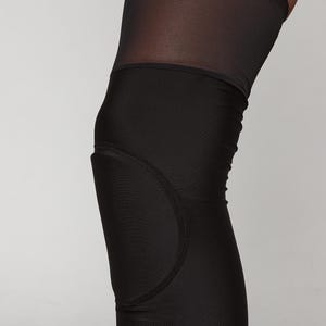 K&ouml;nnte beinhalten: Schwarze Leggings, die bis zum Knie reichen, mit einem Mesh-Einsatz und einem gepolsterten Knieschutz.