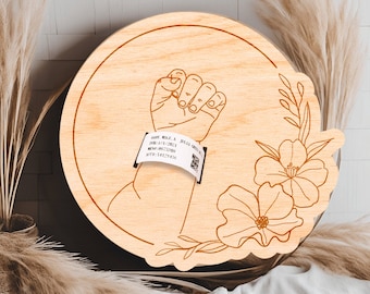 May include: A wooden round plaque with a handprint and a floral design. The handprint has a hospital bracelet with the text "BABY MALL-A, DOB: 1/14/2022, MOM: 08673709, VIP: 58237455".