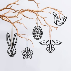 May include: Black geometric Easter ornaments, including a bunny, egg, flower, chicken, and lamb, hang from a gold-painted branch. The ornaments are suspended by strings against a white background, creating a minimalist and festive display.