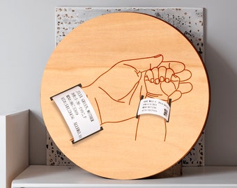 May include: A wooden round plaque with a red line drawing of two hands holding each other. The hands have white paper bands with black text on them. The text on the larger band reads "JILIA GREEN, MOTHER DOB: 5-30-1992, F MC: 54123456 ALLERGY.N".
