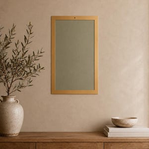 Op de afbeelding: Een rechthoekige wandspiegel met een dunne, matgouden lijst en een saliegroen reflecterend oppervlak. De spiegel is verticaal bevestigd aan een neutrale muur, boven een houten consoletafel met een front van gevlochten riet.