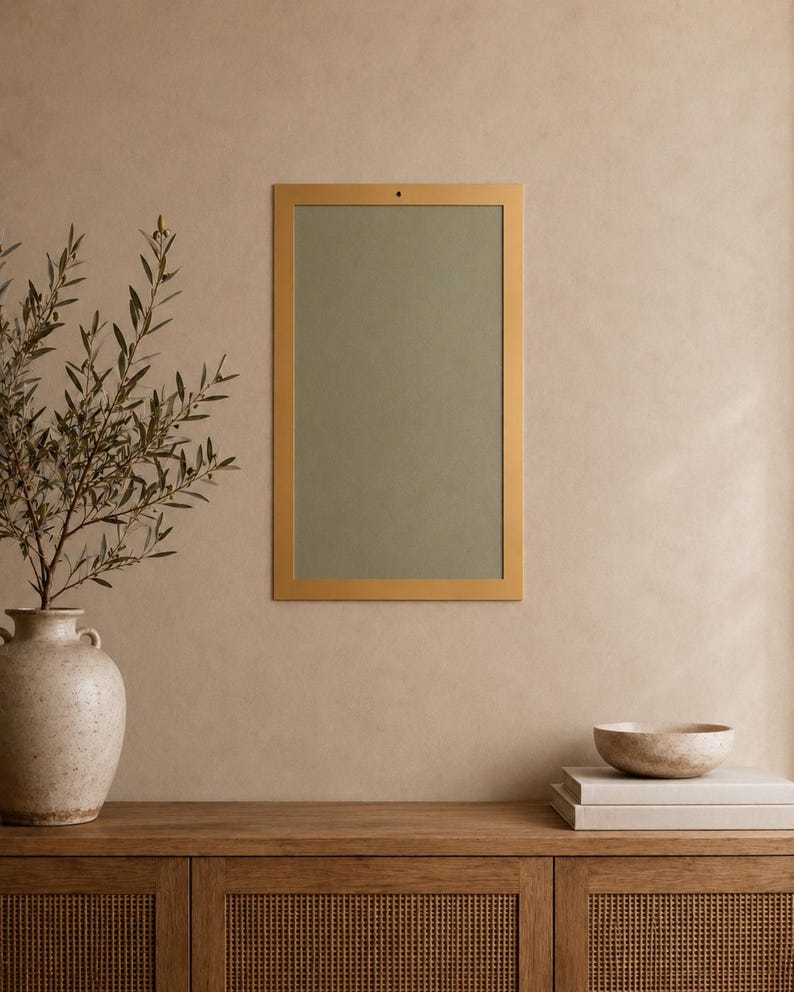 Op de afbeelding: Een rechthoekige wandspiegel met een dunne, matgouden lijst en een saliegroen reflecterend oppervlak. De spiegel is verticaal bevestigd aan een neutrale muur, boven een houten consoletafel met een front van gevlochten riet.