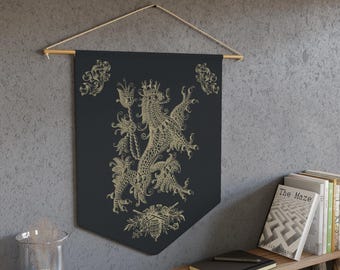 Puede incluir: Un estandarte de pared negro con un diseño de dragón dorado ornamentado. El estandarte está suspendido de una barra de madera con un cordón natural. El dragón es el foco central, rodeado de detalles florales y de volutas. El estandarte está colgado en una pared gris.