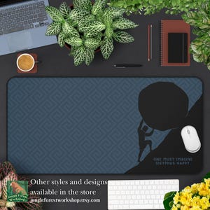 May include: A blue desk mat with a geometric pattern. A silhouette of a person pushing a large rock uphill. The text "ONE MUST IMAGINE SISYPHUS HAPPY." is at the bottom of the mat.