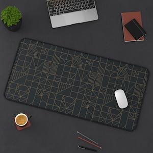 May include: A black desk mat with a geometric pattern in gold. The mat is on a black surface with a laptop, a cup of coffee, pencils, and a computer mouse.