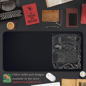 May include: Black desk mat featuring a vintage illustration of a woman reclining in a woodland setting. The illustration is in a silver colour and has an ornate border. The text "Vintage Art Desk Mat" is printed on a red book in the background.