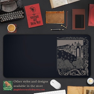 Puede incluir: Una alfombrilla de escritorio rectangular negra con una ilustración detallada de un castillo en un marco decorativo. La alfombrilla tiene el texto "VINTAGE ART DESK MAT". Otros elementos incluyen una máquina de escribir y libros.