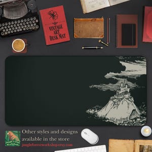 Puede incluir: Una ilustración en blanco y negro de un castillo en la cima de una colina con un fondo verde oscuro. La ilustración está impresa en una alfombrilla de escritorio negra con el texto "Vintage Art Desk Mat" impreso en un libro rojo en el fondo.