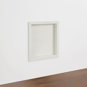 Op de afbeelding: Een witte, verzonken, rechthoekige plank ingebouwd in een witte muur. De plank is leeg en heeft een eenvoudig, strak ontwerp. De muur bevindt zich boven een donkerbruin houten oppervlak.
