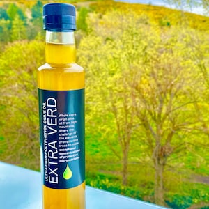May include: A glass bottle of Extra Verd Ultra High Polyphenol Olive Oil. The bottle is clear and shows the golden yellow colour of the olive oil. The label is black with white text that reads "Extra Verd Ultra High Polyphenol Olive Oil" and describes the olive oil as being from high mountains where the challenge of the elements prompts olive trees to make exceptional concentrations of protective micronutrients.