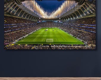 May include: A panoramic view of a large football stadium at night, featuring a bright green pitch surrounded by packed seating tiers. Golden fireworks explode from the roof structure above the field, illuminating the dark sky over the arena.