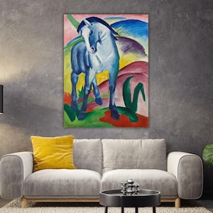May include: An abstract painting of a blue horse with a dark mane and tail, set against a colourful landscape of red, green, yellow, and blue hues. The artwork is displayed on a wall above a grey sofa with a yellow cushion.