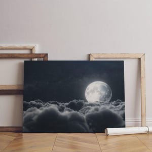 a black and white photo of a full moon above the clouds