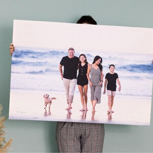 a man holding up a picture of a family on the beach
