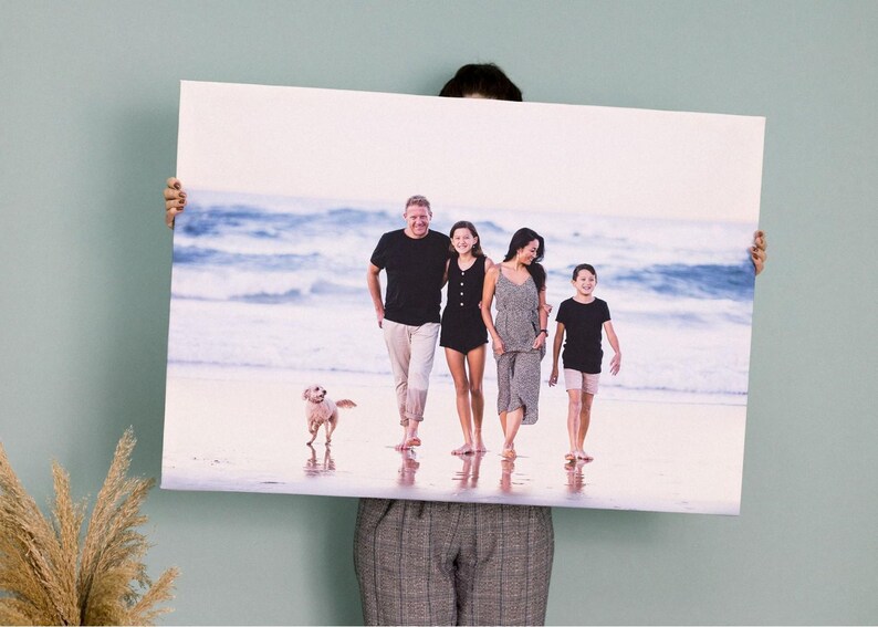a man holding up a picture of a family on the beach