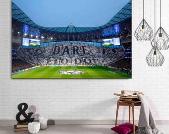 May include: A rectangular wall art print depicting a large football stadium at night with a bright green pitch and a massive crowd in the stands. The crowd displays a large white banner with the black text DARE TO DO across the seating area.