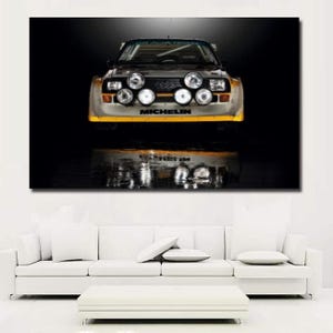 May include: A wall art print featuring a front-facing view of a white rally car with four large circular auxiliary lights mounted on the front bumper. The car displays the Audi logo on the grille and the Michelin brand name in black text.