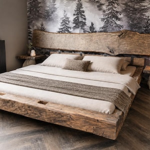 Puede incluir: Una estructura de cama de plataforma baja construida con madera recuperada y un cabecero de borde natural prominente. La cama está vestida con ropa de cama de color beige claro, incluyendo dos almohadas y un camino de cama marrón texturizado, flanqueada por dos mesitas de noche de madera a juego.