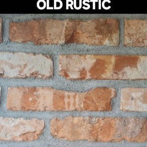 Pode incluir: Close-up de uma parede de tijolos com o texto "OLD RUSTIC" no topo. Os tijolos são retangulares, com uma mistura de cores laranja, castanho e creme. A argamassa é cinza.