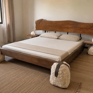 Puede incluir: Una estructura de cama baja de madera marrón oscuro, con un cabecero de borde natural y cuatro grandes bloques de piedra blanca tallada de forma irregular como patas. La cama incluye dos mesitas de noche a juego y ropa de cama beige.