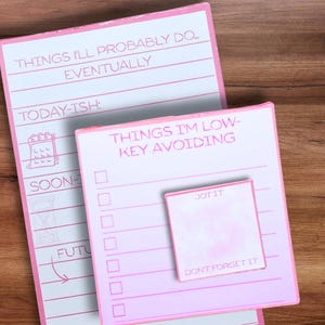 May include: A set of three pink and white paper notepads with printed text. The largest notepad features sections labeled THINGS I'LL PROBABLY DO... EVENTUALLY, TODAY-ISH, SOON-ISH, and FUTURE. A square notepad reads THINGS I'M LOW-KEY AVOIDING.