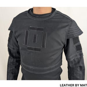 K&ouml;nnte beinhalten: Schwarzes Langarmhemd mit einem quadratischen Design auf der Vorderseite. Das Hemd hat wei&szlig;e N&auml;hte an den R&auml;ndern und an den &Auml;rmeln. Der Text "LEATHER BY MAT" ist am unteren Rand des Bildes sichtbar.