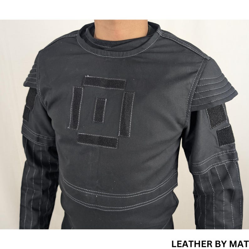 K&ouml;nnte beinhalten: Schwarzes Langarmhemd mit einem quadratischen Design auf der Vorderseite. Das Hemd hat wei&szlig;e N&auml;hte an den R&auml;ndern und an den &Auml;rmeln. Der Text "LEATHER BY MAT" ist am unteren Rand des Bildes sichtbar.