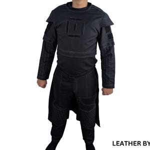 K&ouml;nnte beinhalten: Ein schwarzes Lederkost&uuml;m mit geometrischem Muster auf Brust und &Auml;rmeln. Das Kost&uuml;m hat einen langen Rock und eine Hose. Der Text "LEATHER BY MAT" ist in der rechten unteren Ecke des Bildes sichtbar.