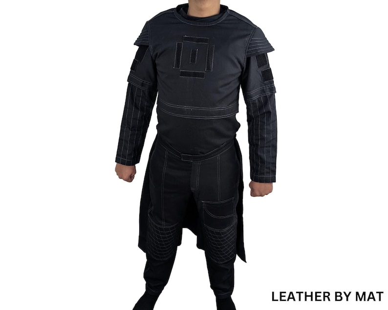 K&ouml;nnte beinhalten: Ein schwarzes Lederkost&uuml;m mit geometrischem Muster auf Brust und &Auml;rmeln. Das Kost&uuml;m hat einen langen Rock und eine Hose. Der Text "LEATHER BY MAT" ist in der rechten unteren Ecke des Bildes sichtbar.