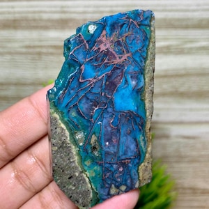 Pode incluir: Uma pedra preciosa polida com cores vibrantes, com tons de azul e turquesa. A pedra apresenta veios castanho-avermelhados na superfície, criando um padrão único. As bordas são cinza e verdes, aumentando seu apelo natural.
