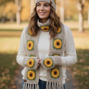 May include: A crocheted hat, scarf, and fingerless gloves set. The beige pieces feature yellow and brown sunflower designs. The scarf has fringe at the bottom. The set is a cozy, handmade accessory.