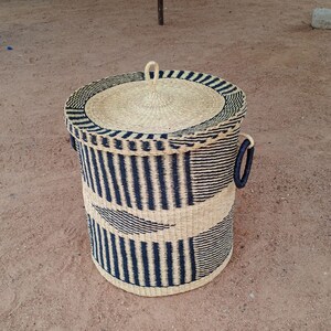 May include: A black and natural woven storage basket with a lid and handles. The basket has a striped pattern.