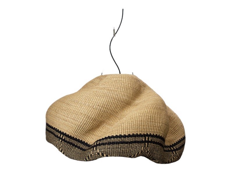 K&ouml;nnte beinhalten: Gewebte Pendelleuchte in Naturbeige mit schwarzem Band am unteren Rand. Der Schirm hat eine unregelm&auml;&szlig;ige Form und wird von einem schwarzen Kabel gehalten.