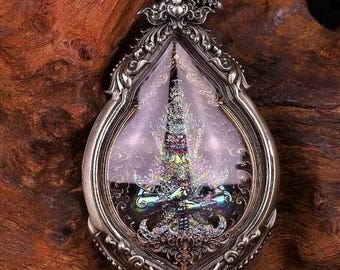 May include: A silver pendant with an ornate design featuring a detailed image of a deity inside a glass oval. The pendant is surrounded by small stones.