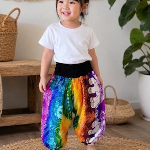 Könnte beinhalten: Ein schlichtes weißes T-Shirt mit kurzen Ärmeln kombiniert mit einer weiten, regenbogenfarbenen Hose mit schwarzem Gummibund. Die Hose zeigt ein lebhaftes Farbverlaufsmuster mit detaillierten weißen Elefantenmotiven und floralen Mandalas.
