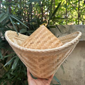 May include: A woven bamboo basket with a wide, flat brim and a conical top. The basket is made of natural, light brown bamboo and has a traditional design.