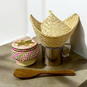 May include: A set of woven bamboo kitchenware, including a round bowl with a lid, a larger bowl with a lid, and a wooden spoon. The bowls are made of natural woven bamboo and have a light brown color.