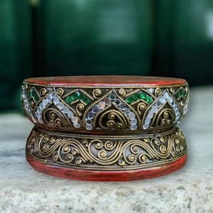 May include: A red wooden pedestal with gold and green decorative trim. The trim features intricate designs and small white beads.