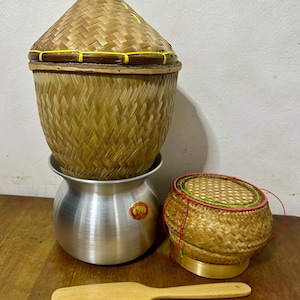 May include: A set of three woven bamboo baskets with lids, one with a metal pot underneath. The baskets are brown with yellow and red accents. A wooden spatula is also included.