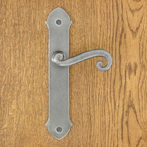 Könnte beinhalten: Ein silberfarbener Türgriff aus Metall mit einer langen, rechteckigen Grundplatte mit spitzen Enden und zwei Schraublöchern. Der Griff selbst hat eine geschwungene, ergonomische Form mit einer dekorativen Spirale am Ende für den Halt.