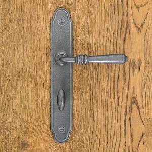 Peut inclure: Une poignée de porte en métal gris foncé avec une plaque rectangulaire aux extrémités arrondies, fixée par deux vis à tête plate. La poignée horizontale présente une prise cylindrique nervurée et un petit bouton ovale est situé en dessous.