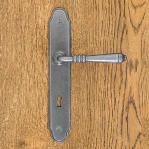 Könnte beinhalten: Ein mattgrauer Türdrücker aus Metall mit einer langen, rechteckigen Langschildplatte mit abgerundeten Enden, einem horizontalen Hebel mit drei Zierringen und einem Standard-Schlüsselloch, befestigt durch zwei sichtbare Schrauben oben und unten.
