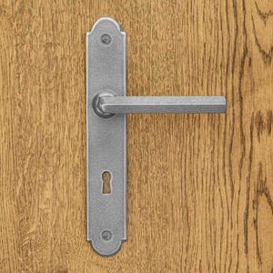 Könnte beinhalten: Ein silberfarbener Türgriff aus Metall mit einer rechteckigen Grundplatte mit abgerundeten Enden, einem horizontalen Hebel und einem Schlüsselloch. Der Beschlag ist mit zwei sichtbaren Schrauben oben und unten auf einer hellen Holzoberfläche befestigt.
