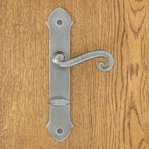 Peut inclure: Une poignée de porte en métal argenté avec une plaque arrière rectangulaire aux extrémités pointues et deux trous de vis. La poignée présente une forme incurvée en volute avec une extrémité arrondie et un petit bouton ovale horizontal.