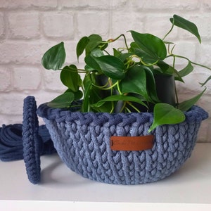 Può includere: Un portavasi in crochet blu con un'etichetta in pelle marrone che dice "Casa Fresca". Il portavasi contiene una pianta in vaso con foglie verdi.