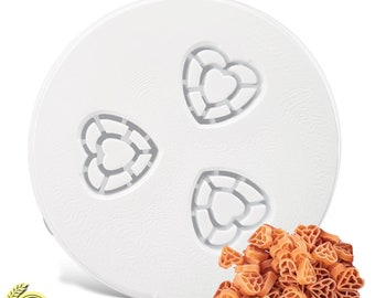 May include: White plastic pasta maker attachment with three heart-shaped molds. A pile of cooked heart-shaped pasta is in the foreground.